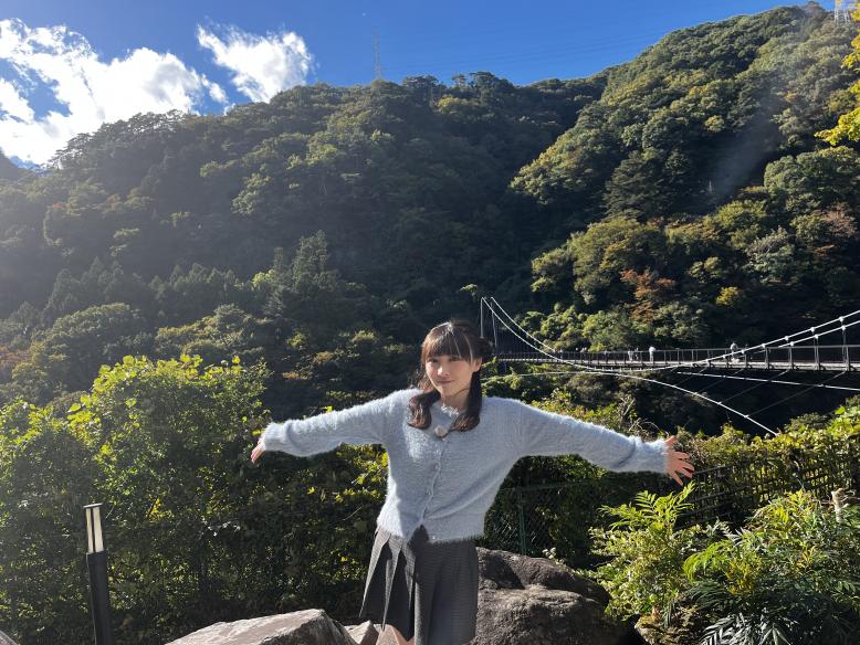 吊り橋と雄大な自然をバックに手を広げる高瀬さん