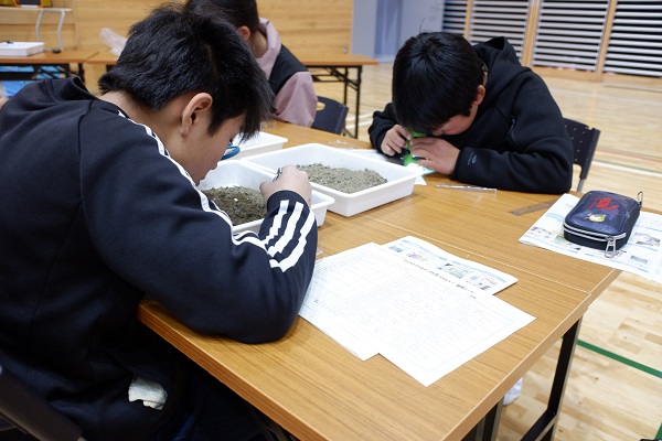 川原の土砂の中からプラスチックだと思うものを探す様子